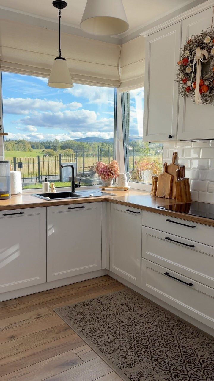 White kitchen cabinetry with black handles and light wood countertops near a window.