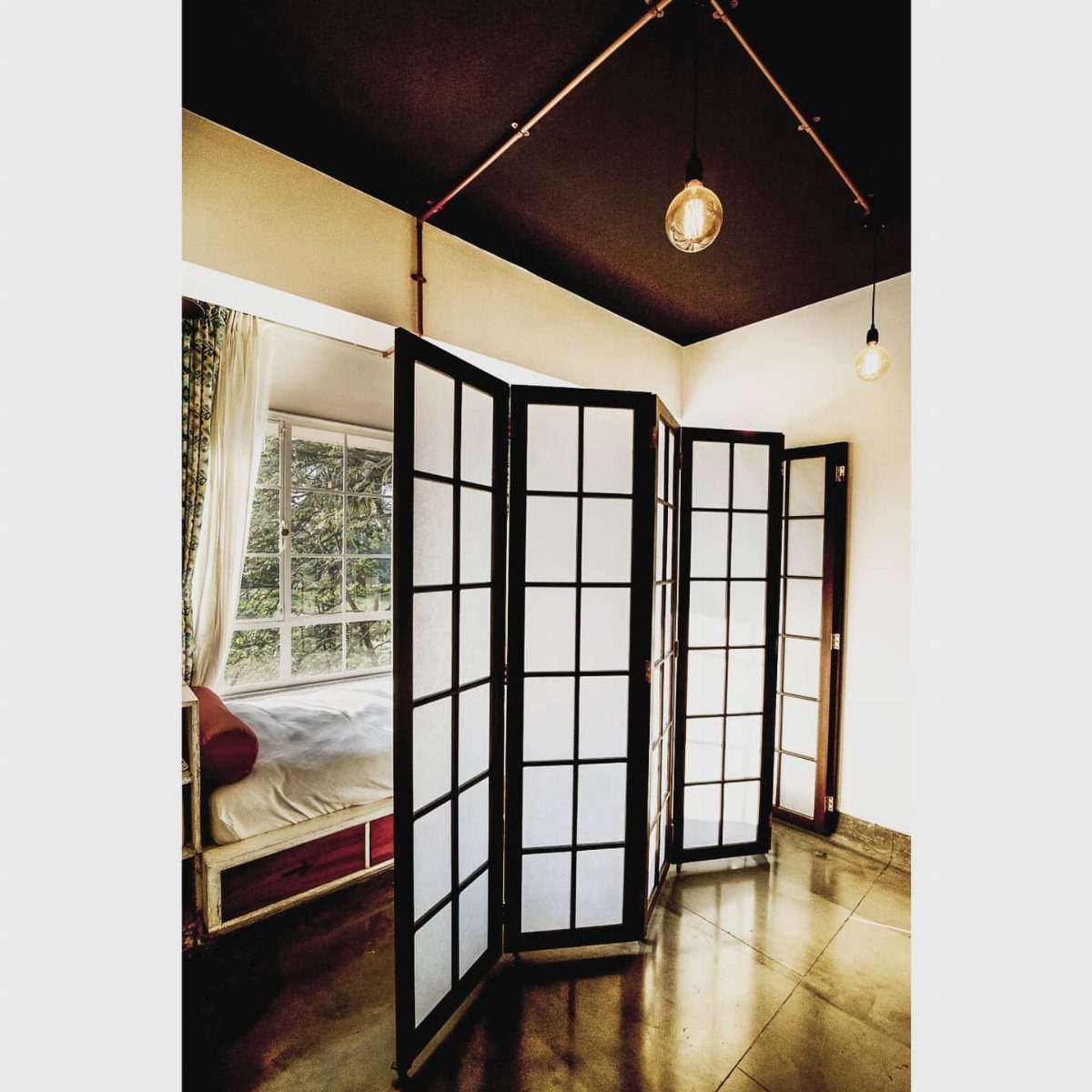 Black-framed Japanese shoji screen dividing a bedroom with white walls and dark ceiling.